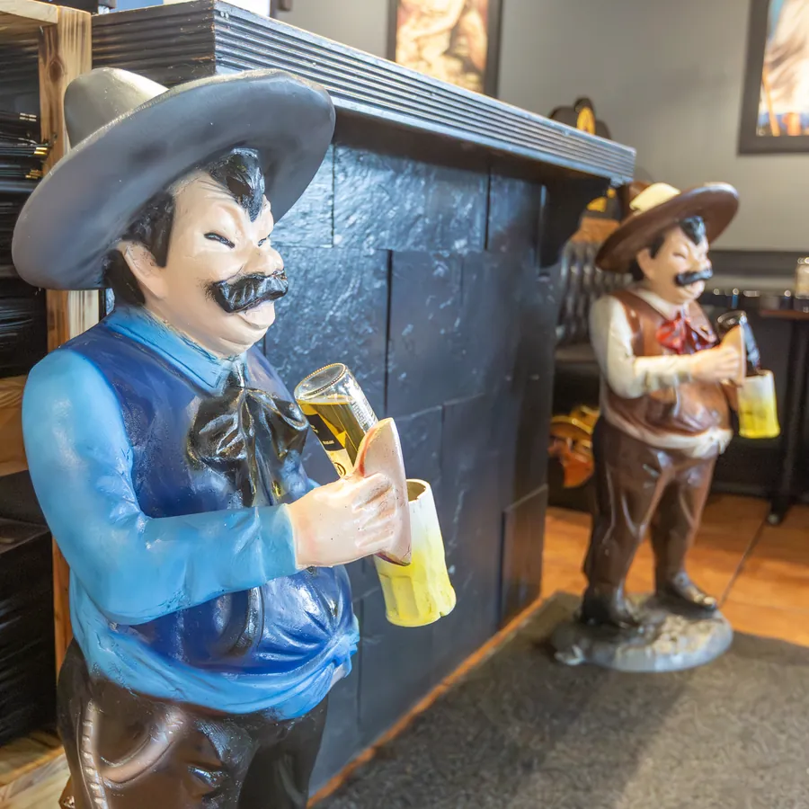 Two hand-painted charro statues holding beer mugs beside the El Toreado host stand
